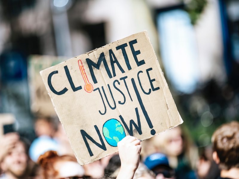 Sign with Climate Justice Now written on it being held up at a protest